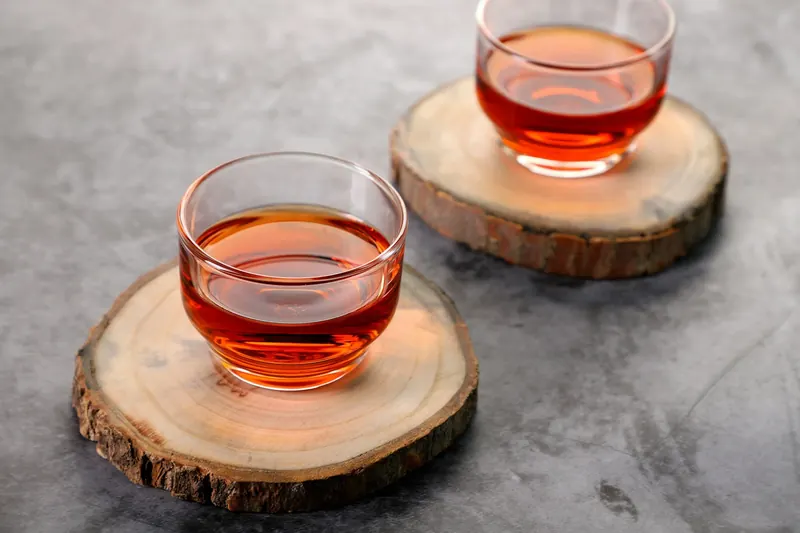 Two glass cups of amber Klara Tea on wooden coasters